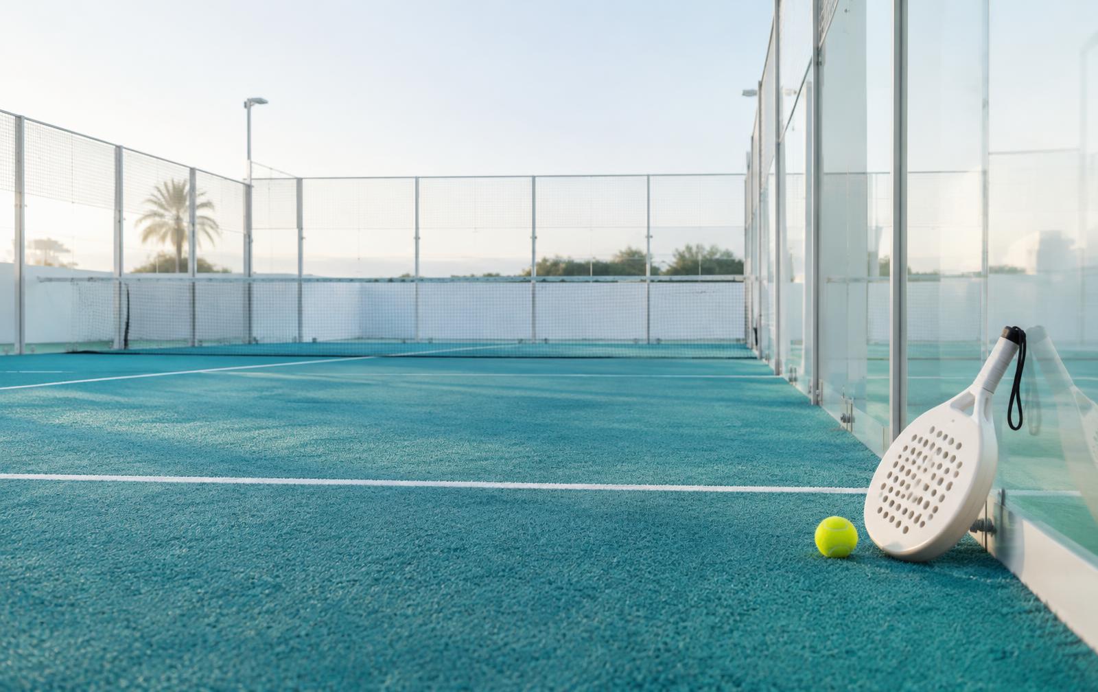 Cancha de pádel con césped turquesa, raqueta blanca y bola